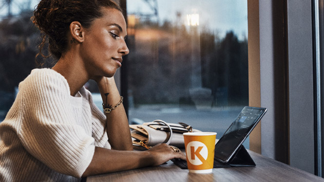 Woman looking at her tablet, drinking Circle K Coffee