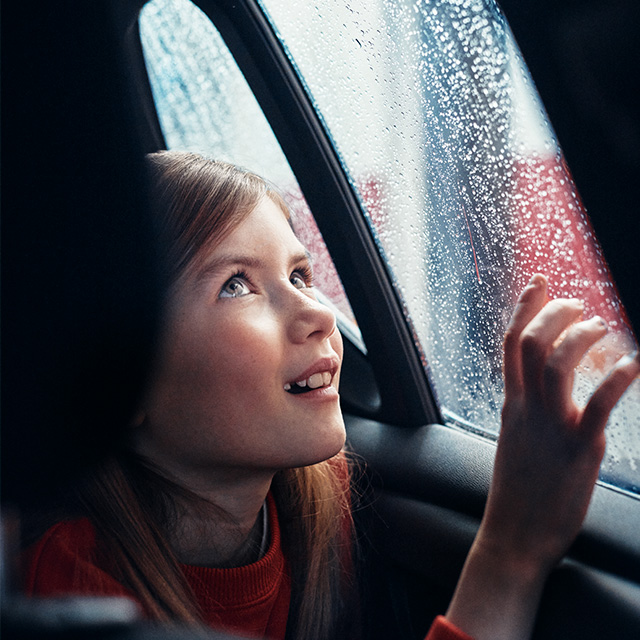 A girl sitting in a car during a Circle K car wash, gazing out of the window