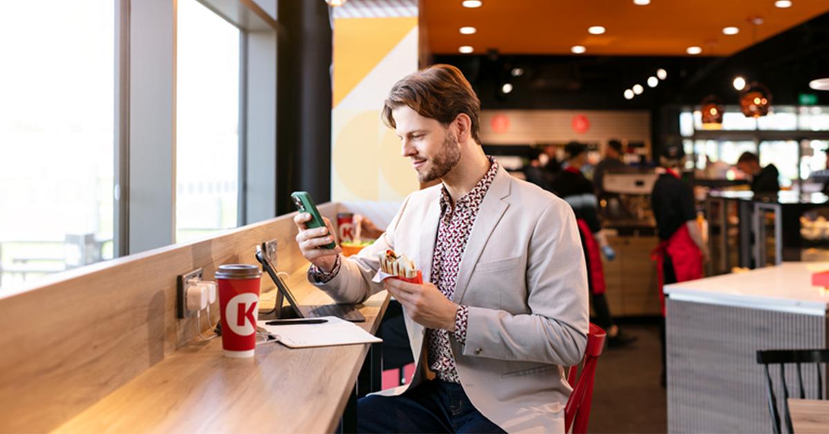 A guy eating on a Circle K station while checking his phone